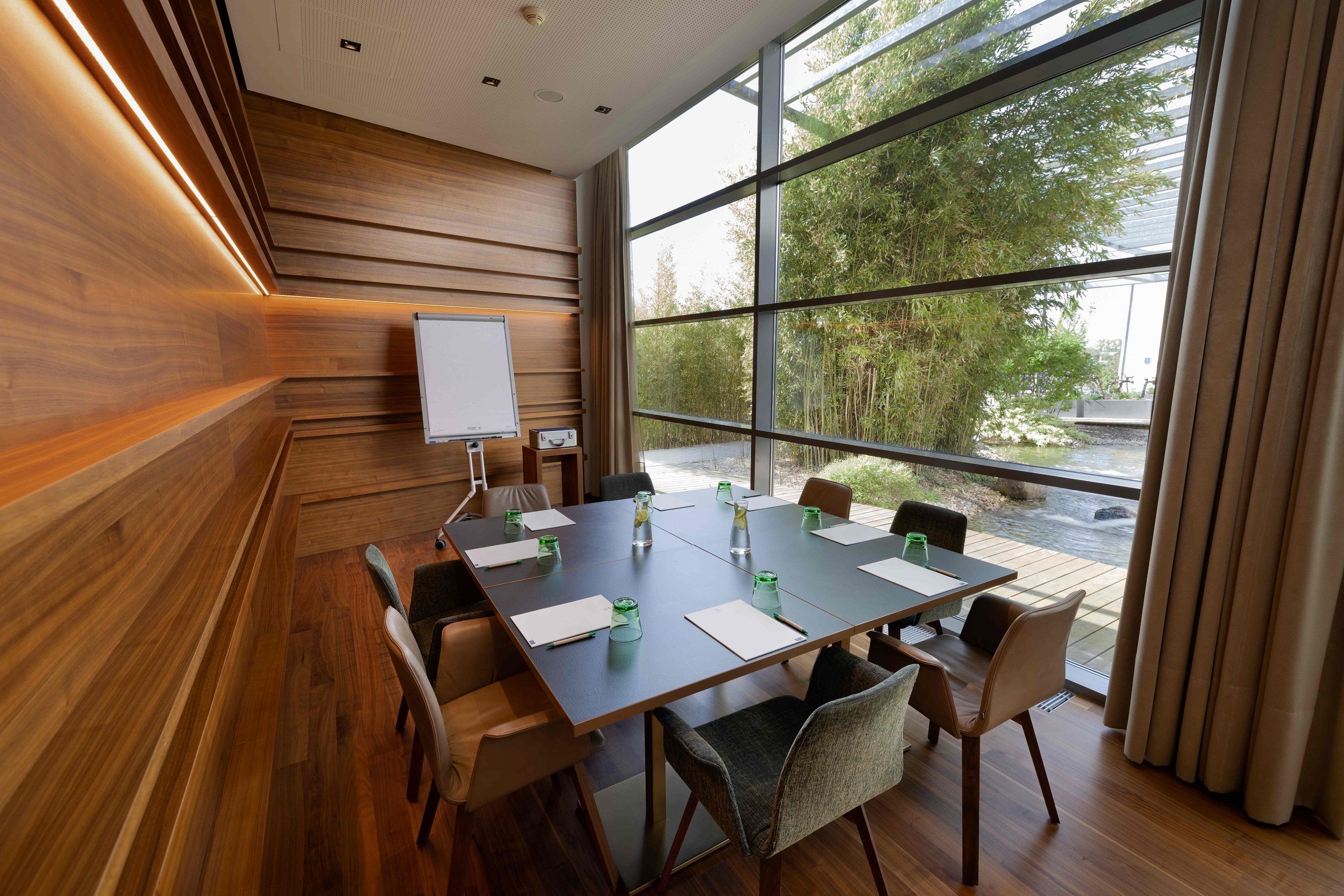 Modern meeting room with wooden walls, large table and view of a garden.