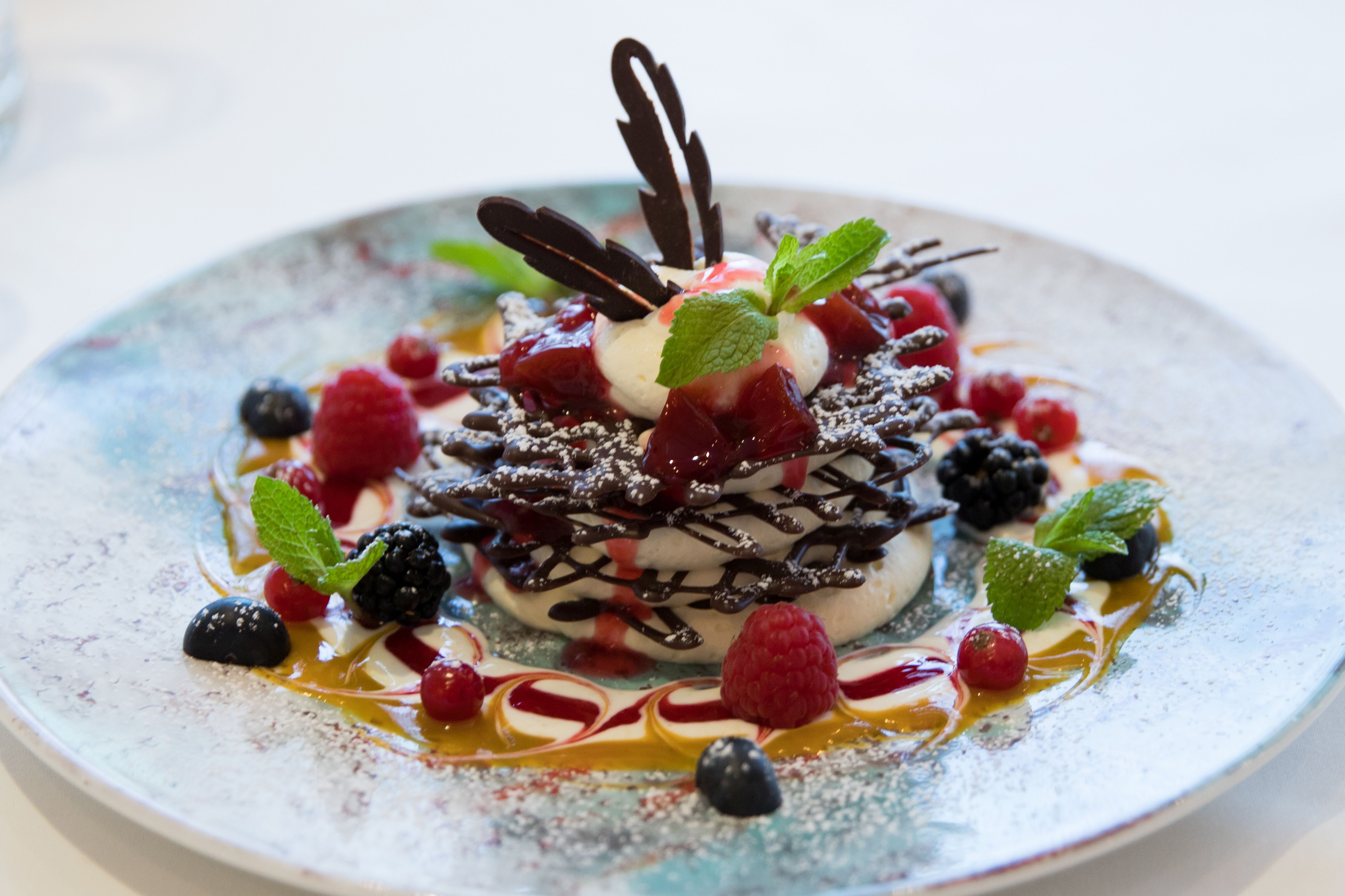 An artfully arranged dessert with chocolate, cream, berries and mint leaves on a plate.