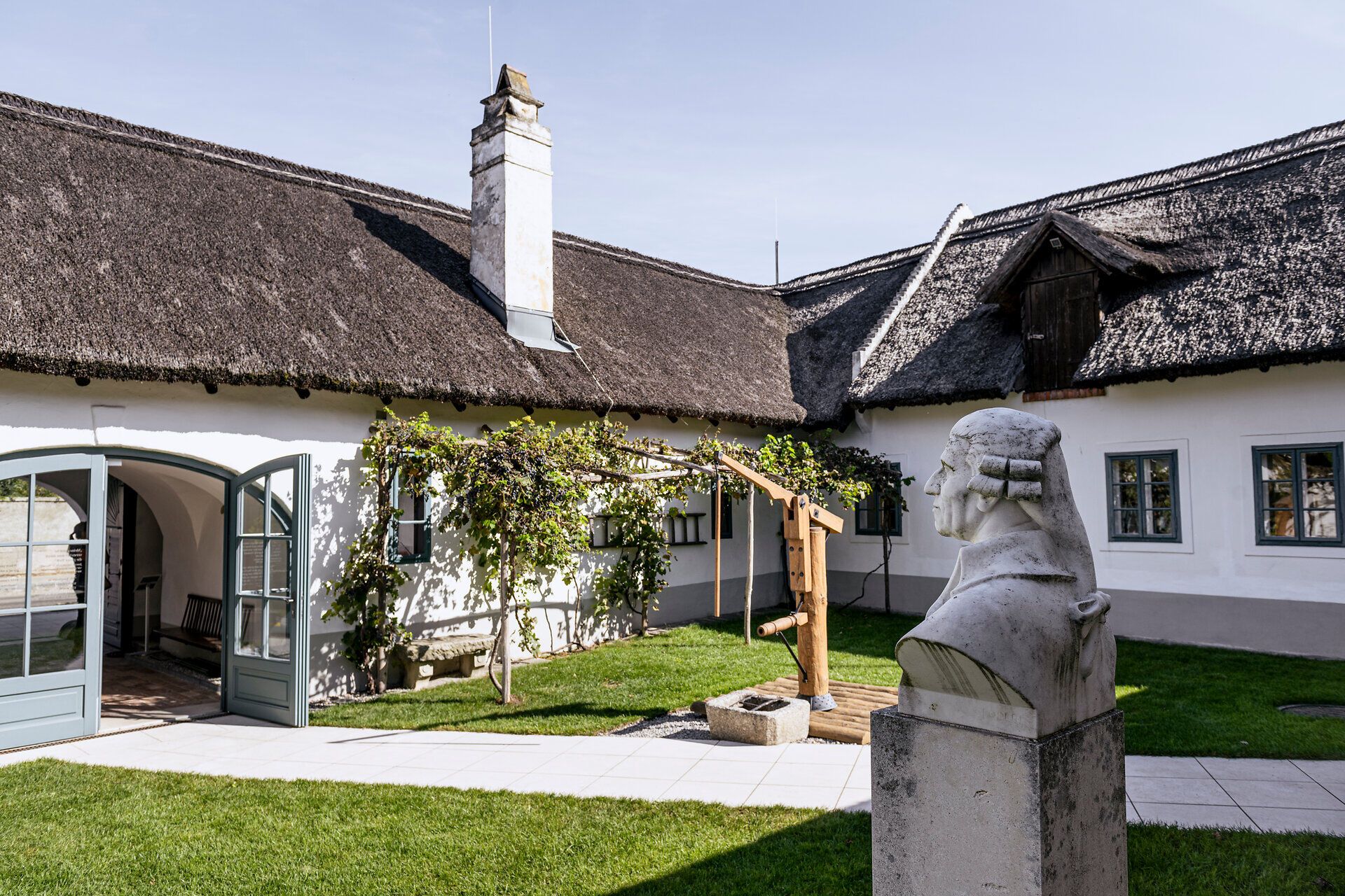 Inner courtyard of Haydn's birthplace with thatched roofs and a bust of Haydn.