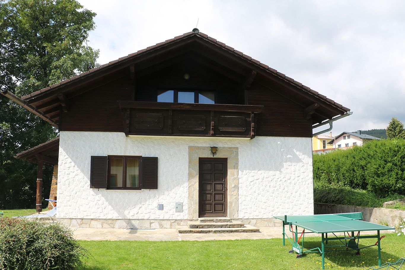 A white house with a wooden balcony and table tennis table in the garden.
