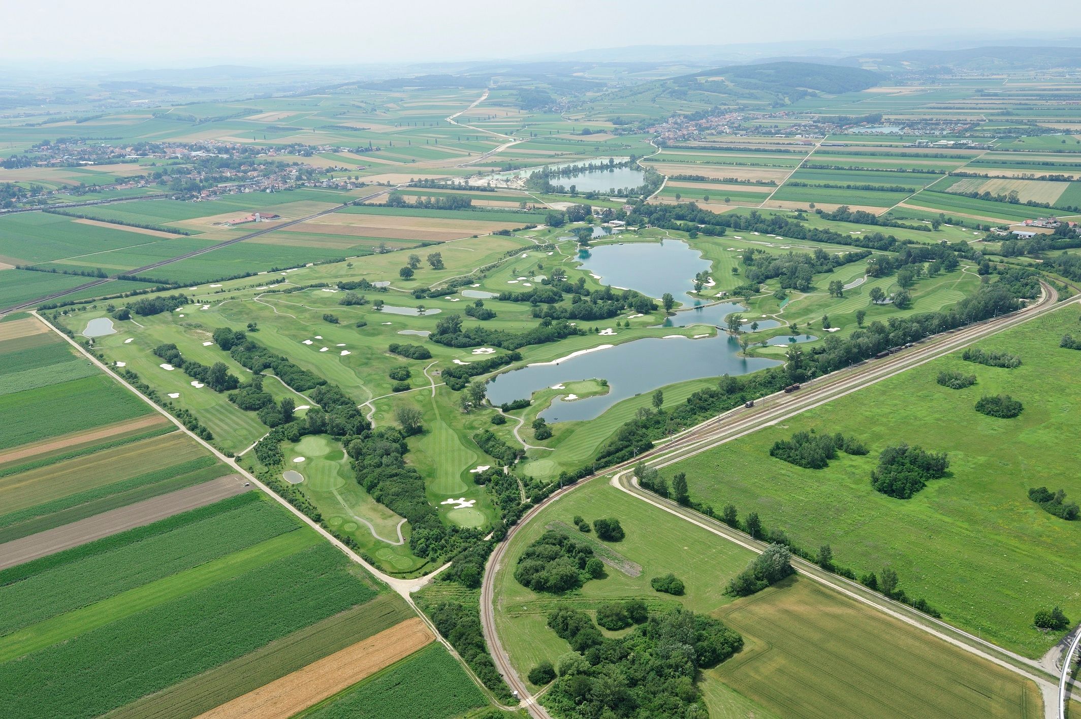 Aerial view of a golf course with lakes and surrounding fields.