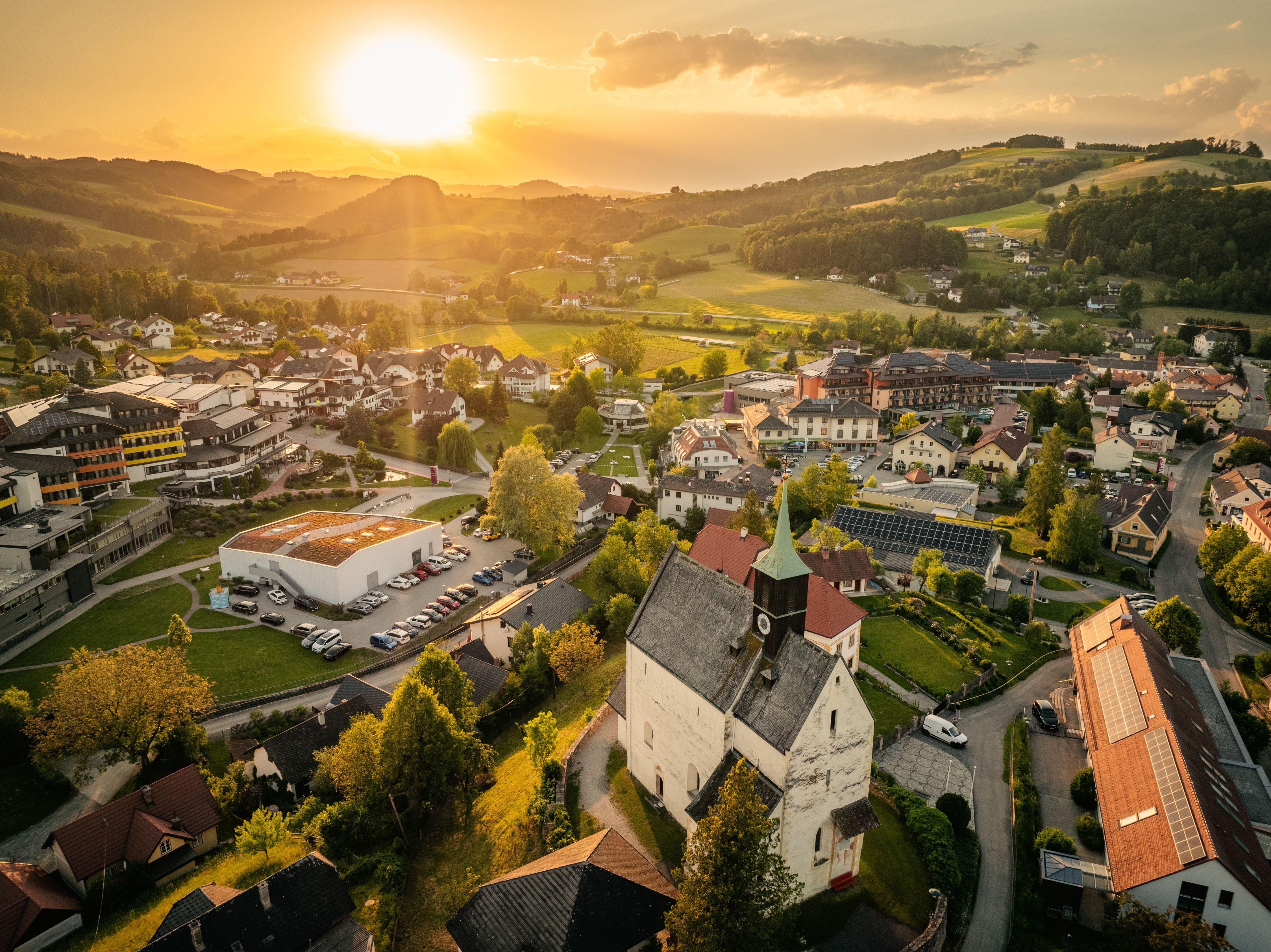 Aerial view of Bad Schönau at sunset, with the fortified church in the foreground and hills in the background.