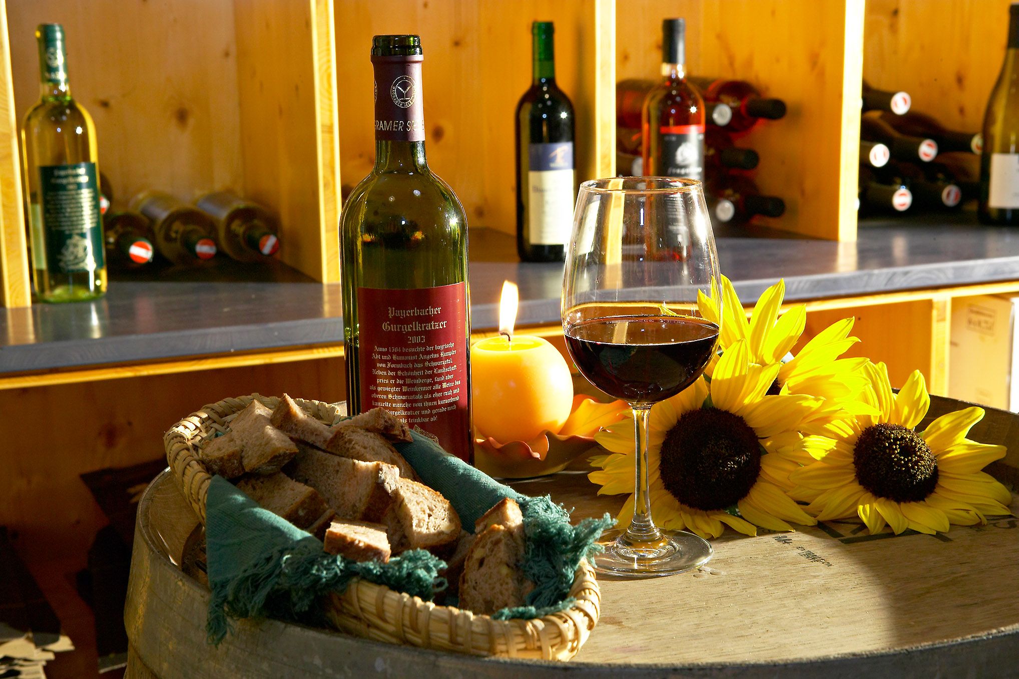 Wine bottle and glass on a barrel with bread and sunflowers.