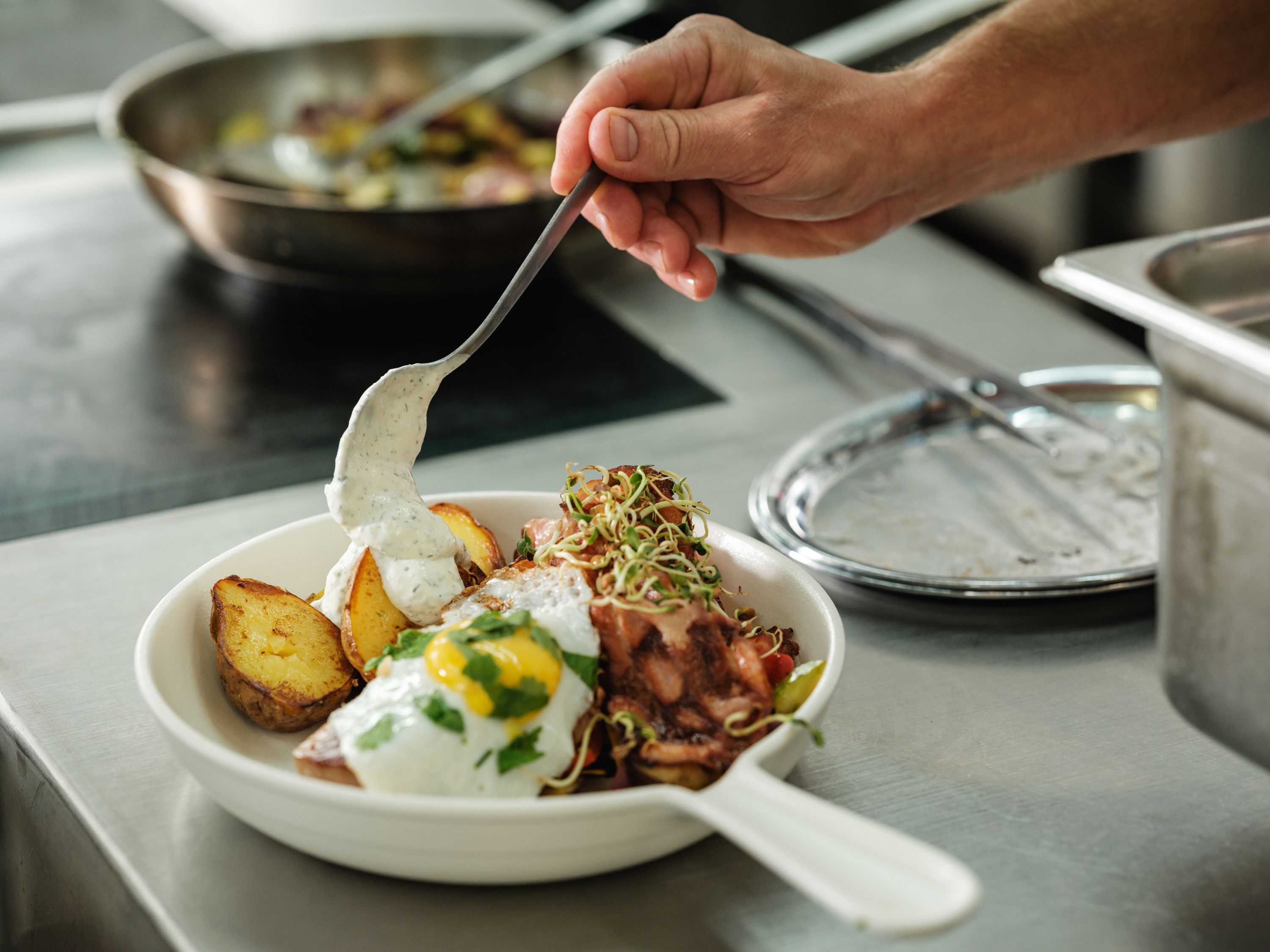A plate with fried potatoes, fried egg and sauce is served in a kitchen.