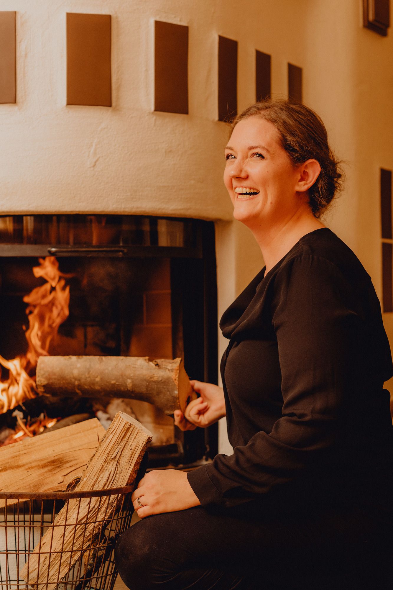 Woman smiling in front of a fireplace with a burning fire.