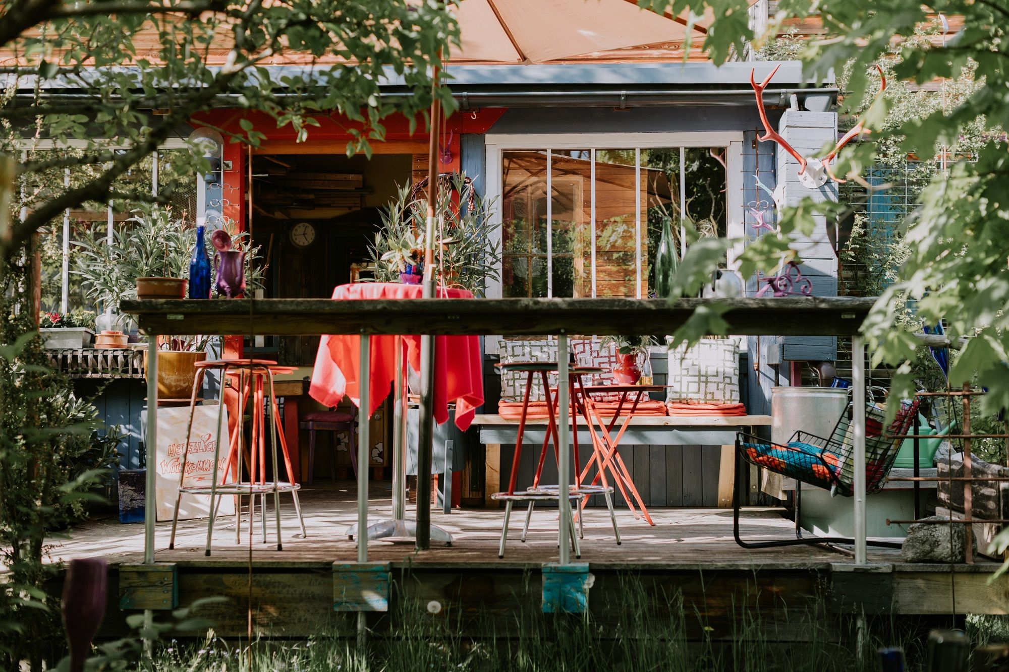 Colorful terrace in front of the location with red chairs and table, surrounded by plants and decorations.