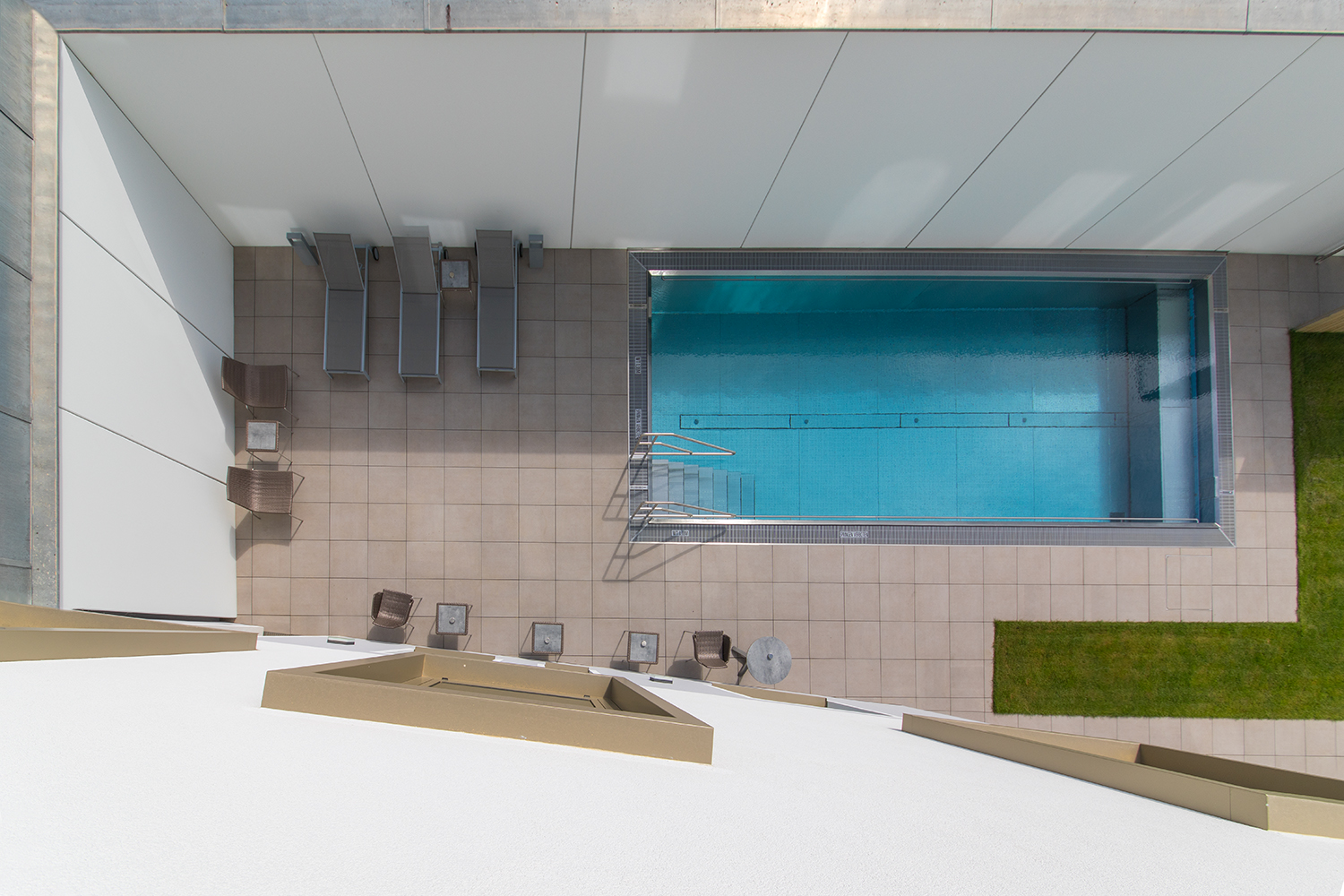 Top view of a rectangular pool with sun loungers and tables on a tiled terrace.