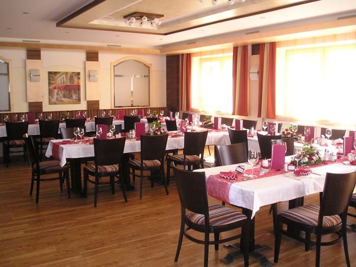 An elegantly decorated dining room with several tables, red table runners and chairs.