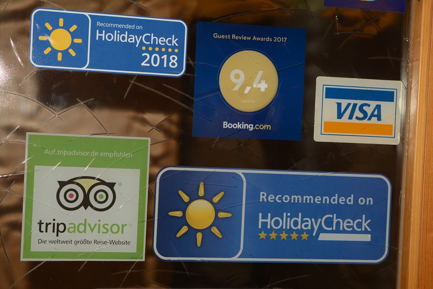 Stickers from HolidayCheck, Booking.com, TripAdvisor and Visa on a glass surface.