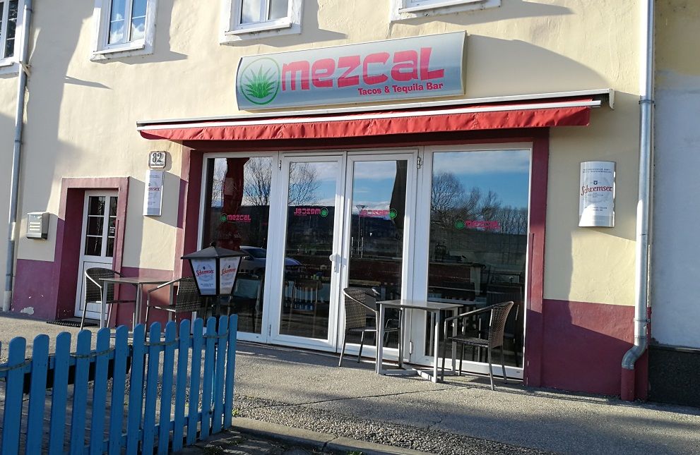 Exterior view of the Mezcal Restaurant with red awnings and seating.