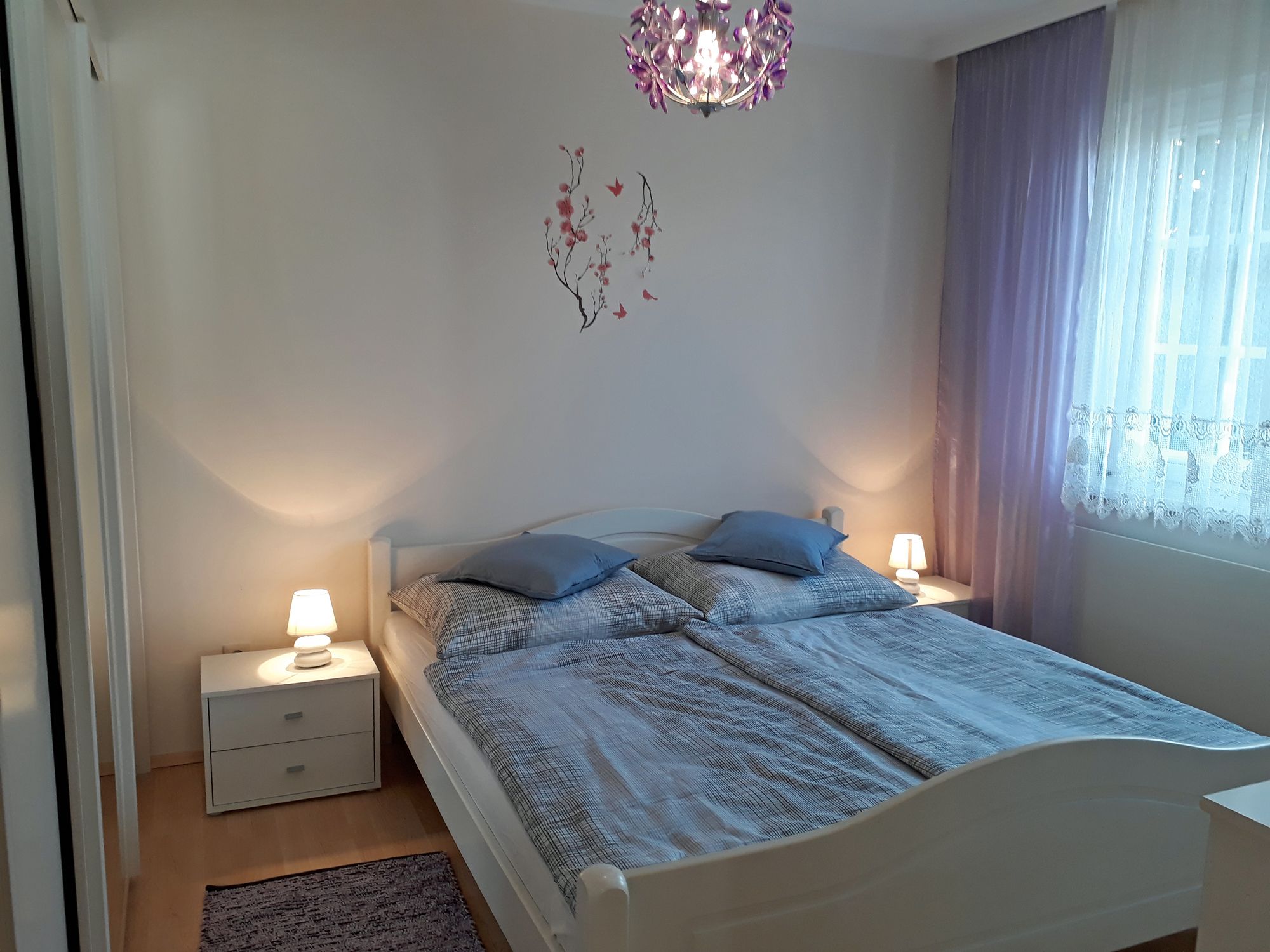 A cozy bedroom with a double bed, two bedside tables with lamps and purple curtains.