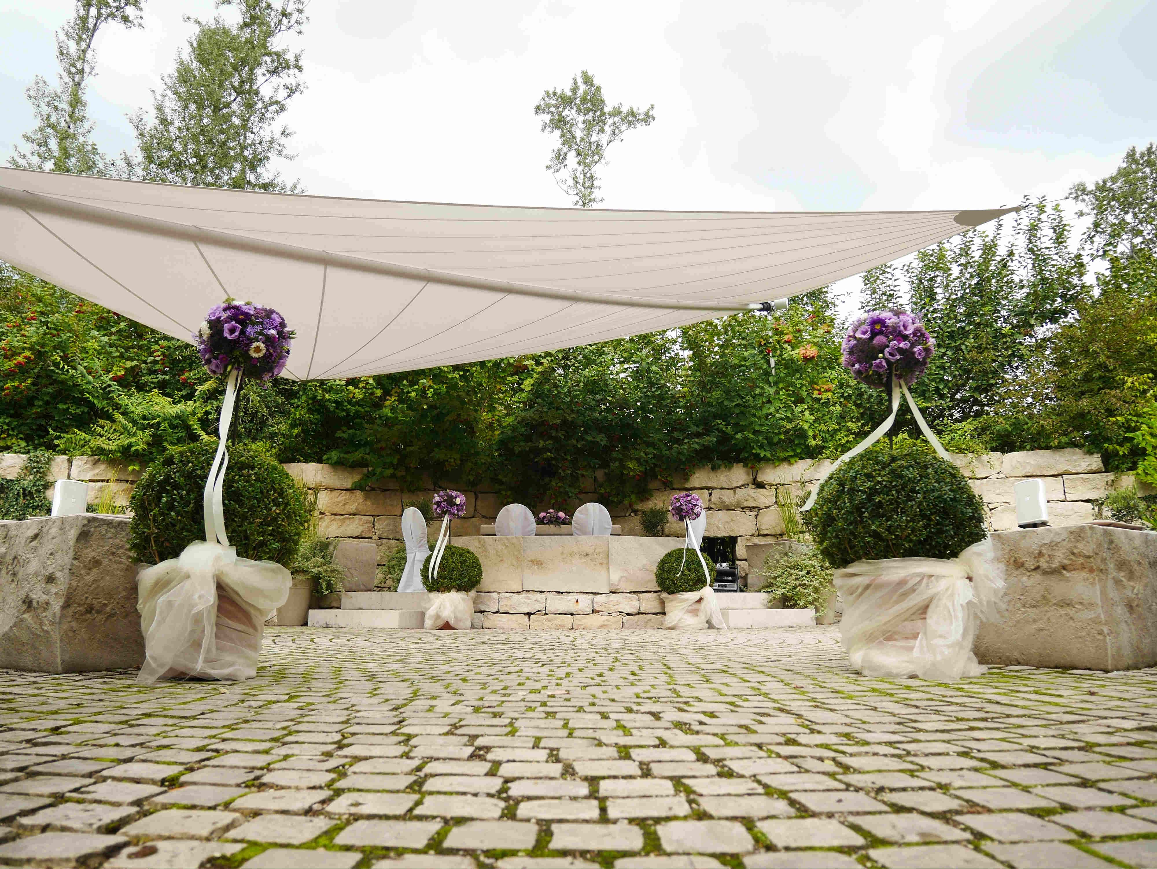 Outdoor wedding decoration with purple flowers and white chairs.