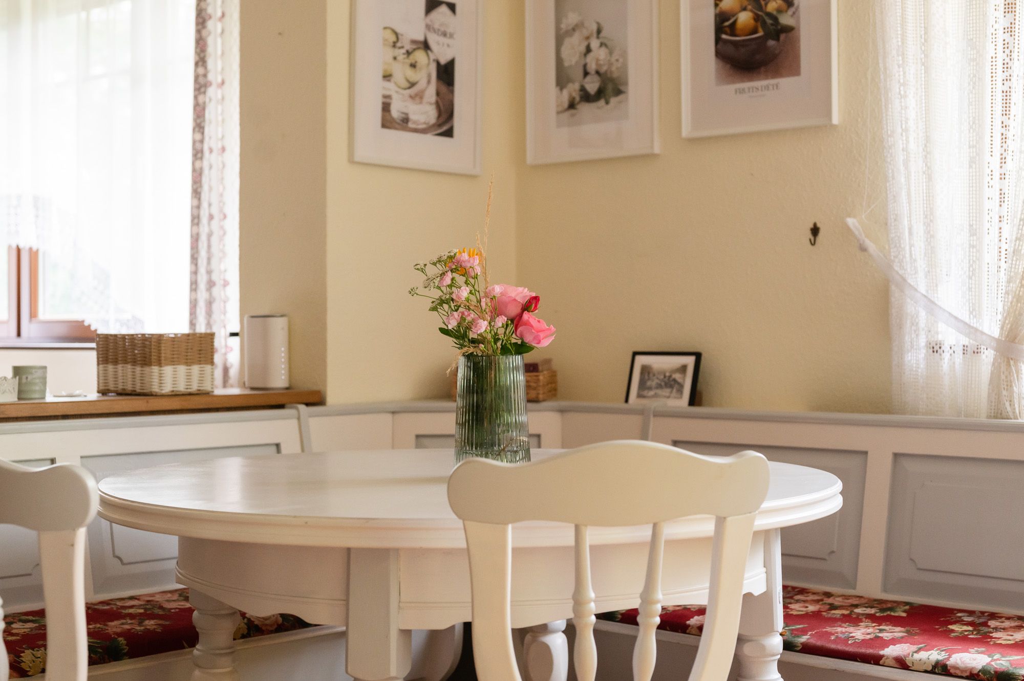 Dining area in a vacation home with round table, bouquet of flowers in a vase and decorative pictures on the wall.