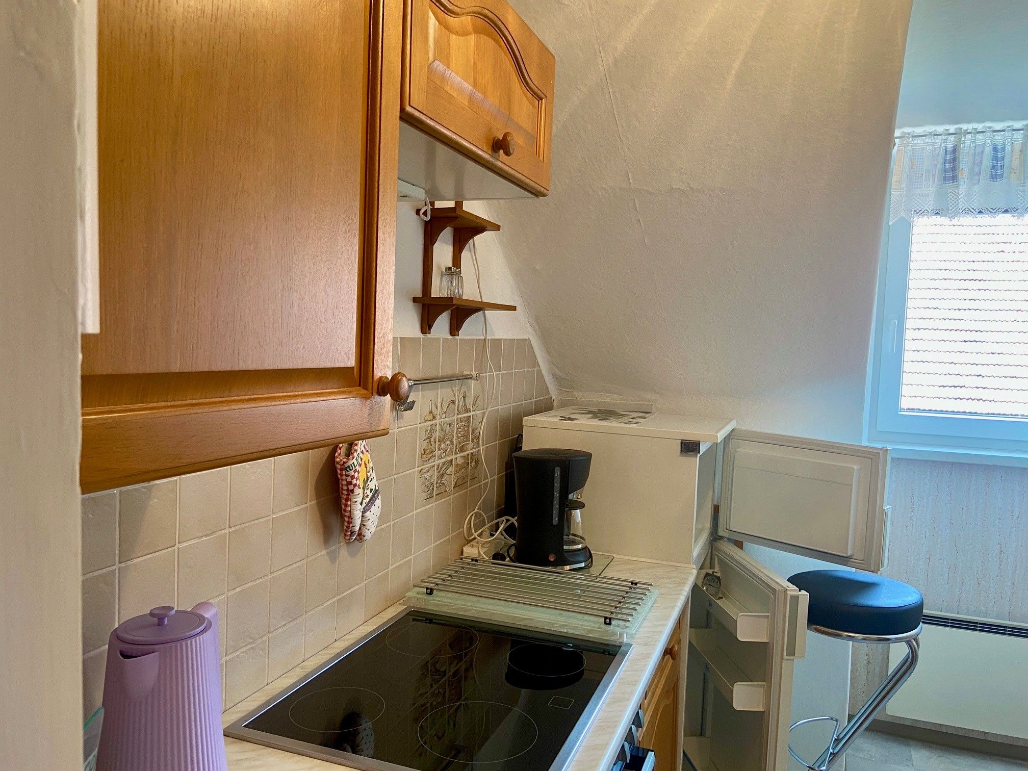 Small kitchen with wooden cupboards, stove, coffee machine and open fridge.