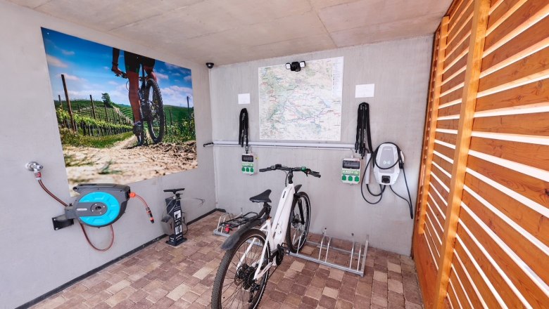 Bicycle in a garage with charging stations and mural of a cyclist in a vineyard.