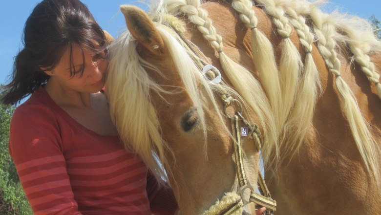 A woman in a red sweater stands next to a horse with a braided mane.