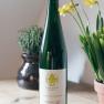 A bottle of Gr&uuml;ne Veltliner wine sits on a table next to yellow flowers and a pot of herbs.