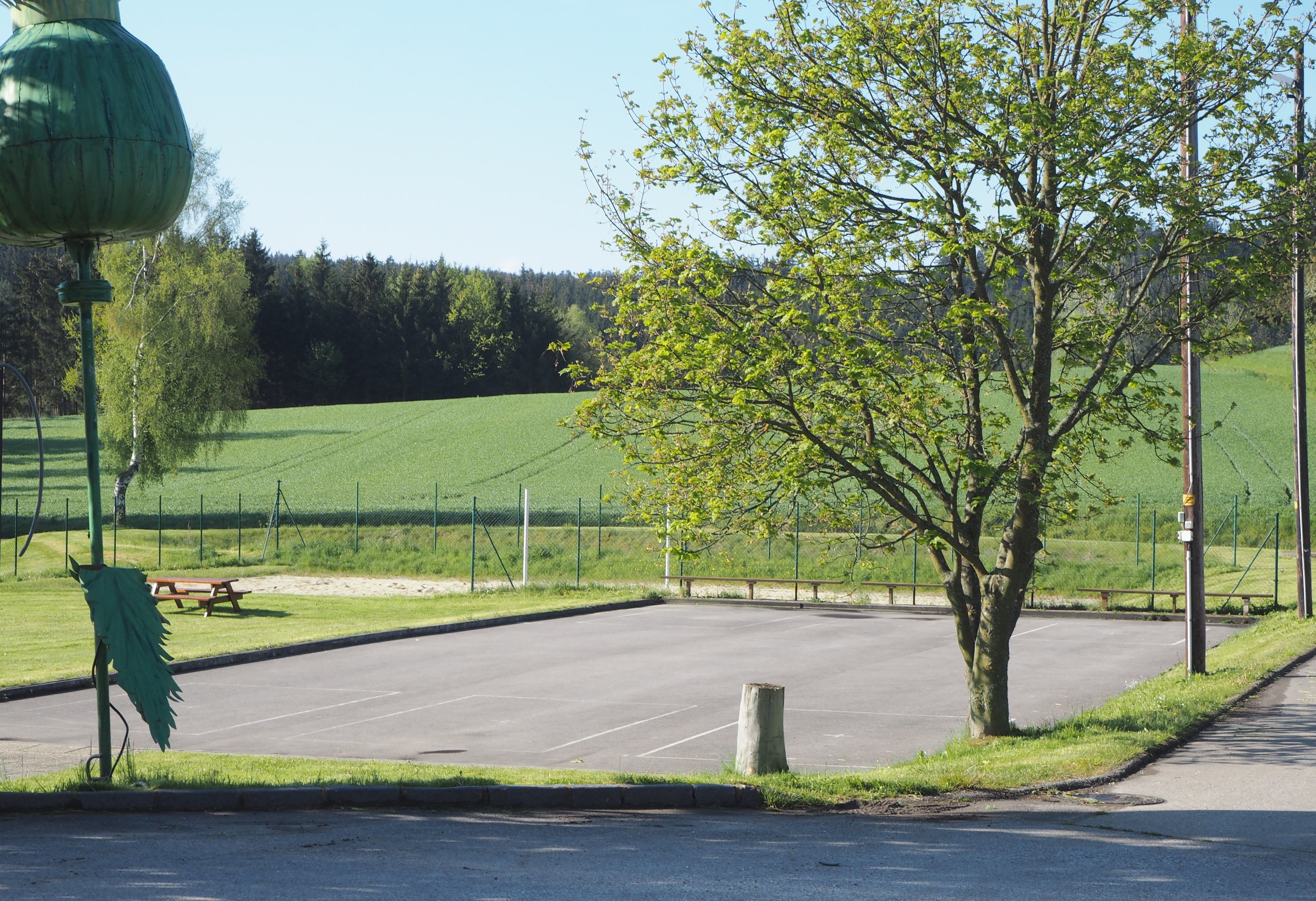 Asphalt court with tree and volleyball court in the background.