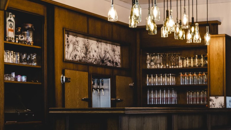 A cozy bar with a wooden interior and hanging bottle lamps.