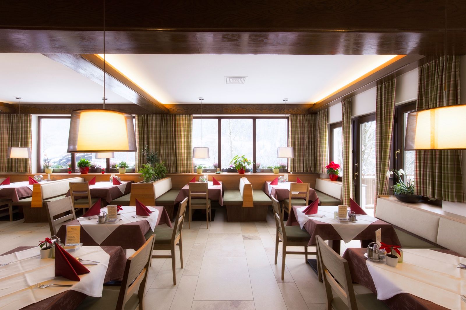 Interior view of a cozy restaurant with wooden furniture, laid tables and large windows.