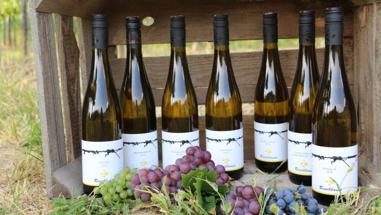 Seven bottles of wine in a wooden crate with grapes in the foreground.