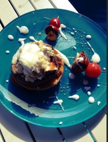 A blue plate with a dessert consisting of pancakes, cream and cherries on a table.