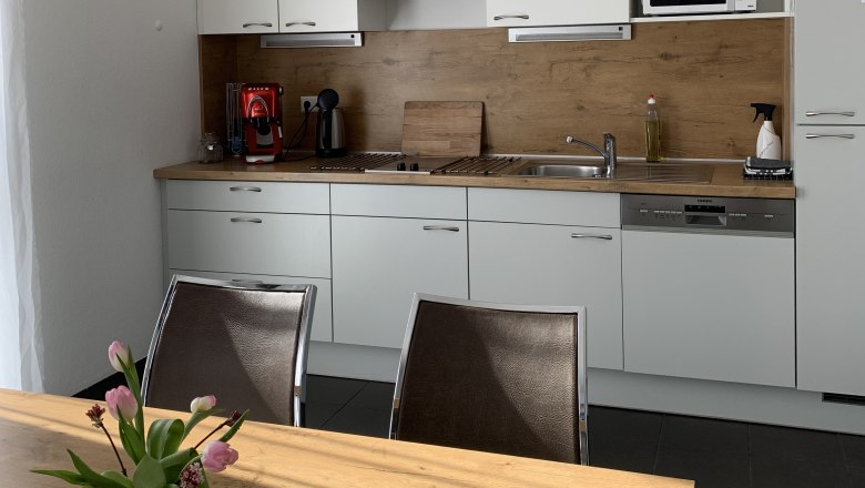 Modern kitchen unit with white cupboards, wooden worktop, coffee machine and microwave. A table with a bouquet of flowers in the foreground.