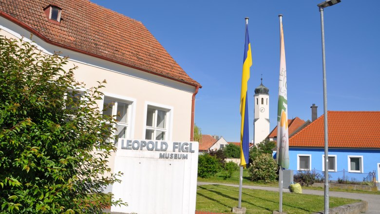 Leopold Figl Museum with flags and church tower in the background.