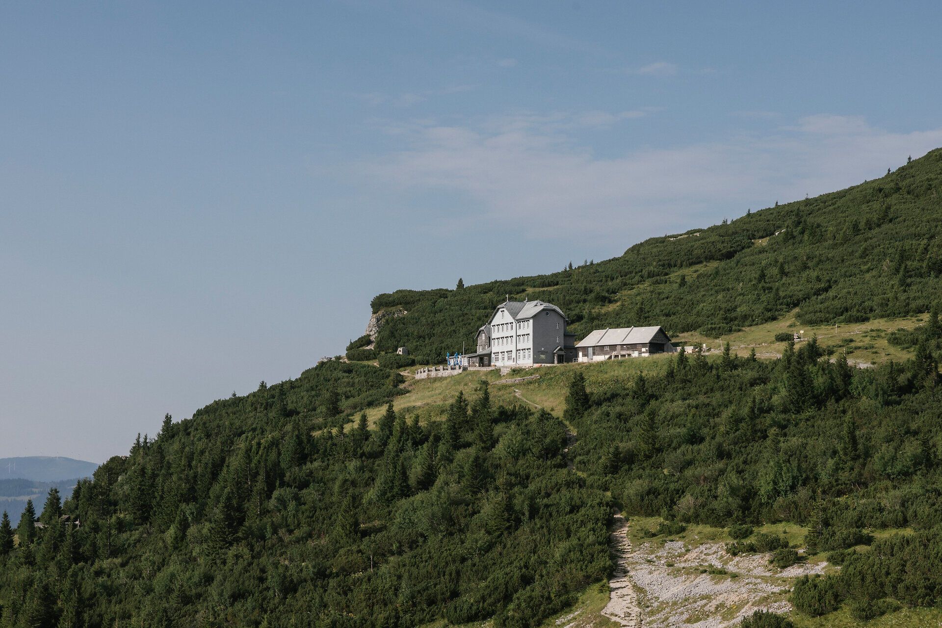 A panoramic view of the Ottohaus on the Rax, nestled among forested mountain slopes