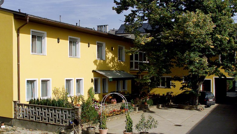 Private room Holzer family, © Fam. Holzer Yellow building with several windows, plants in the foreground and a large tree next to it.