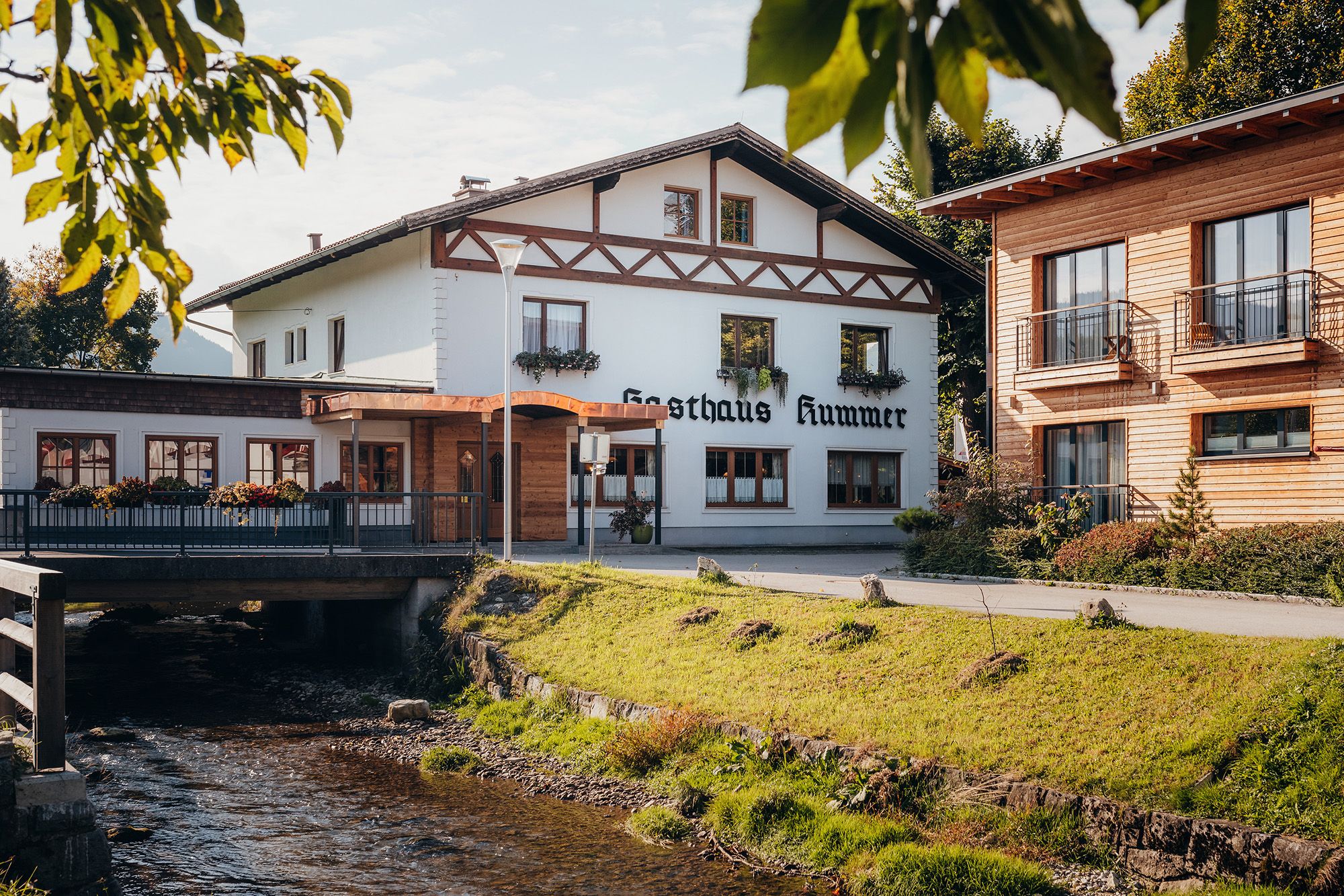 A traditional inn with a white façade and wooden decorations next to a stream.