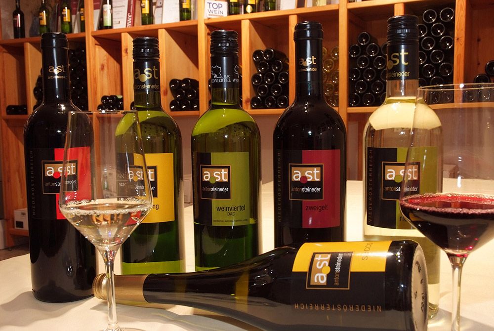 Various wine bottles and glasses on a table in a wine cellar.