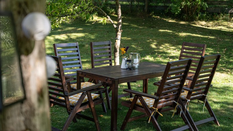 Garden with wooden table and chairs, decorated with flowers and candles.