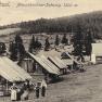 Historical photograph of wooden huts on the Mönichkirchner Schwaig, surrounded by forest and meadows, with people in the foreground.