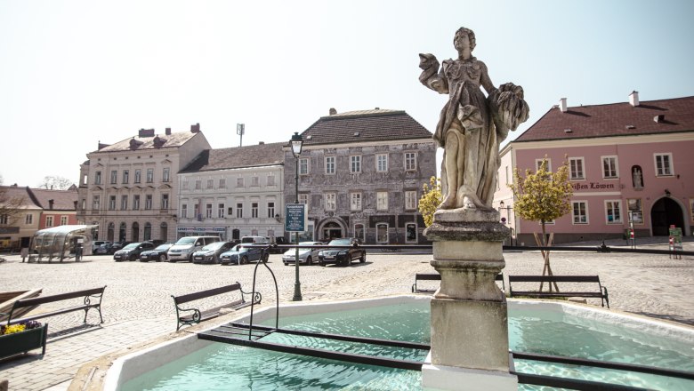 sgrafit Hotel, © Astrid Bartl A square with a statue in a fountain, surrounded by historic buildings and parked cars.
