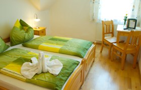 Cozy guest room with double bed, green bed linen and wooden furniture.