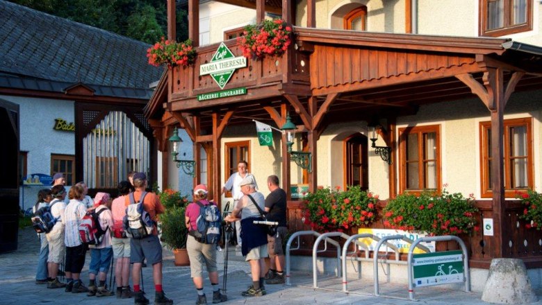 A group of hikers stands in front of the Café Maria Theresia with its wooden veranda and floral decorations.