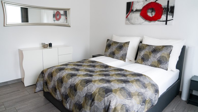 Modern bedroom with double bed, abstract artwork and mirror.