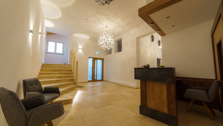 Modern reception with wooden counter, two gray armchairs and stairs.