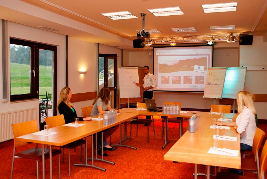 Wienerwaldhof Seminar Hotel: Seminar room equipped with a presentation system, flip charts, and four participants seated at tables.