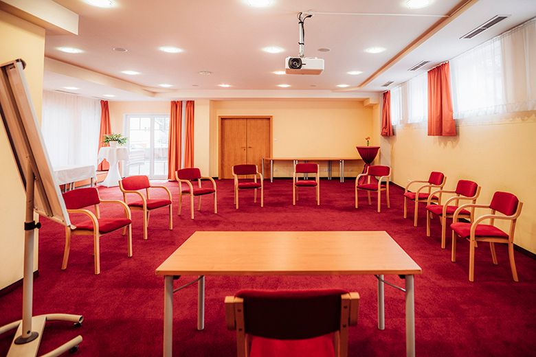 A seminar room with a red carpet, circle of chairs, table, flipchart and projector.