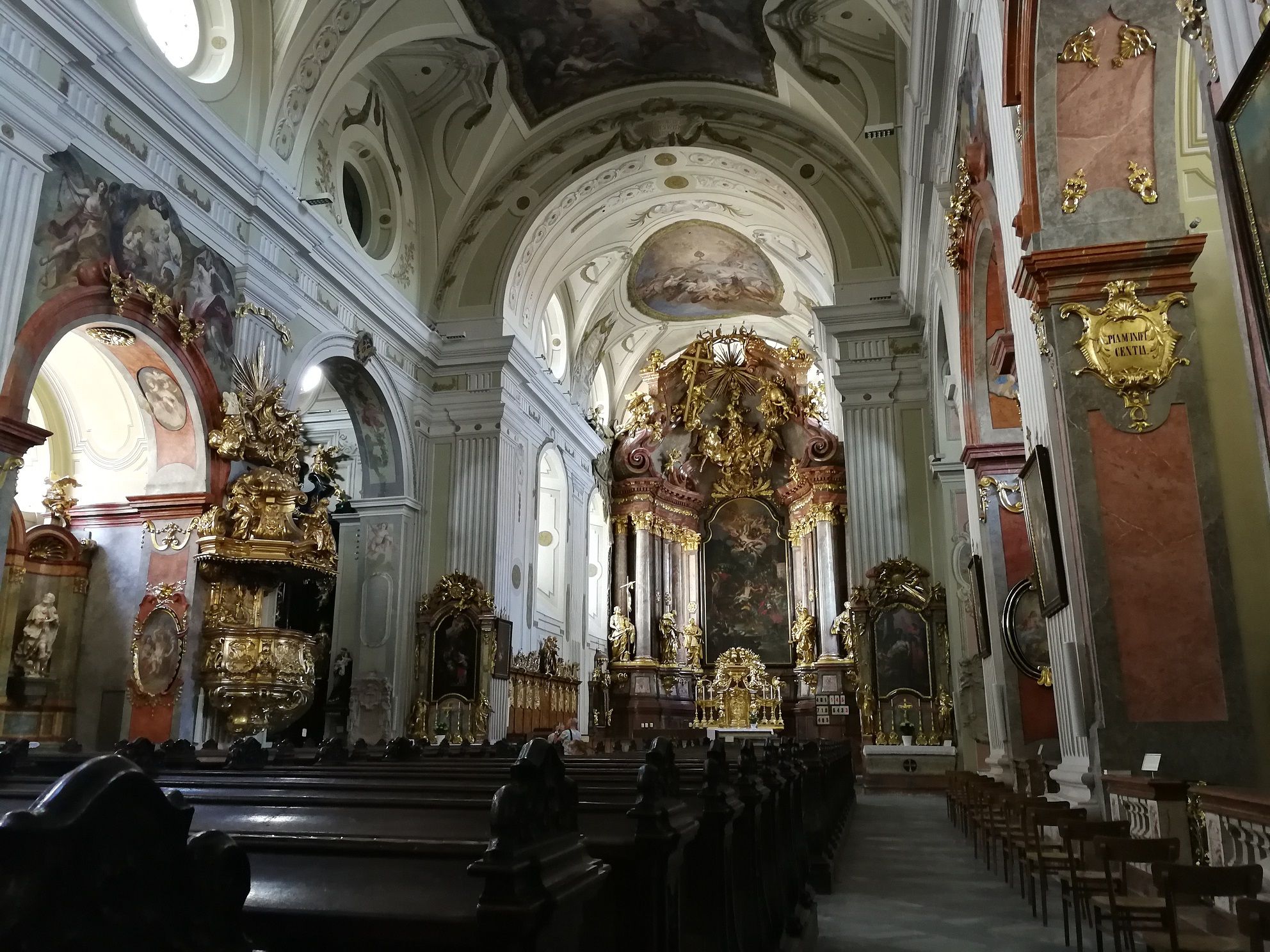 Interior view of a baroque church with a richly decorated altar and frescoes.