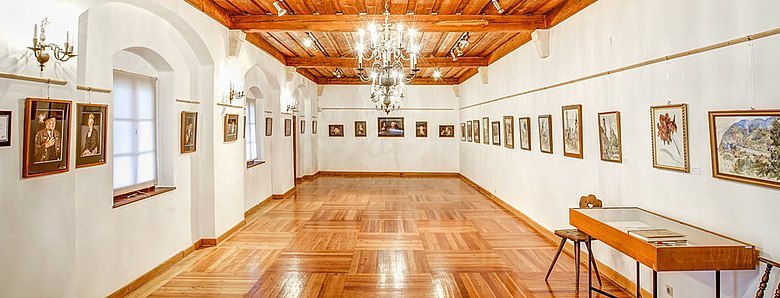 An elegant showroom with a wooden floor, white walls and paintings on the walls.
