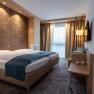 Modern hotel room with double bed, wooden paneling and windows with curtains.