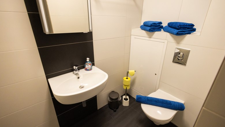 Modern bathroom with washbasin, toilet and blue towels.