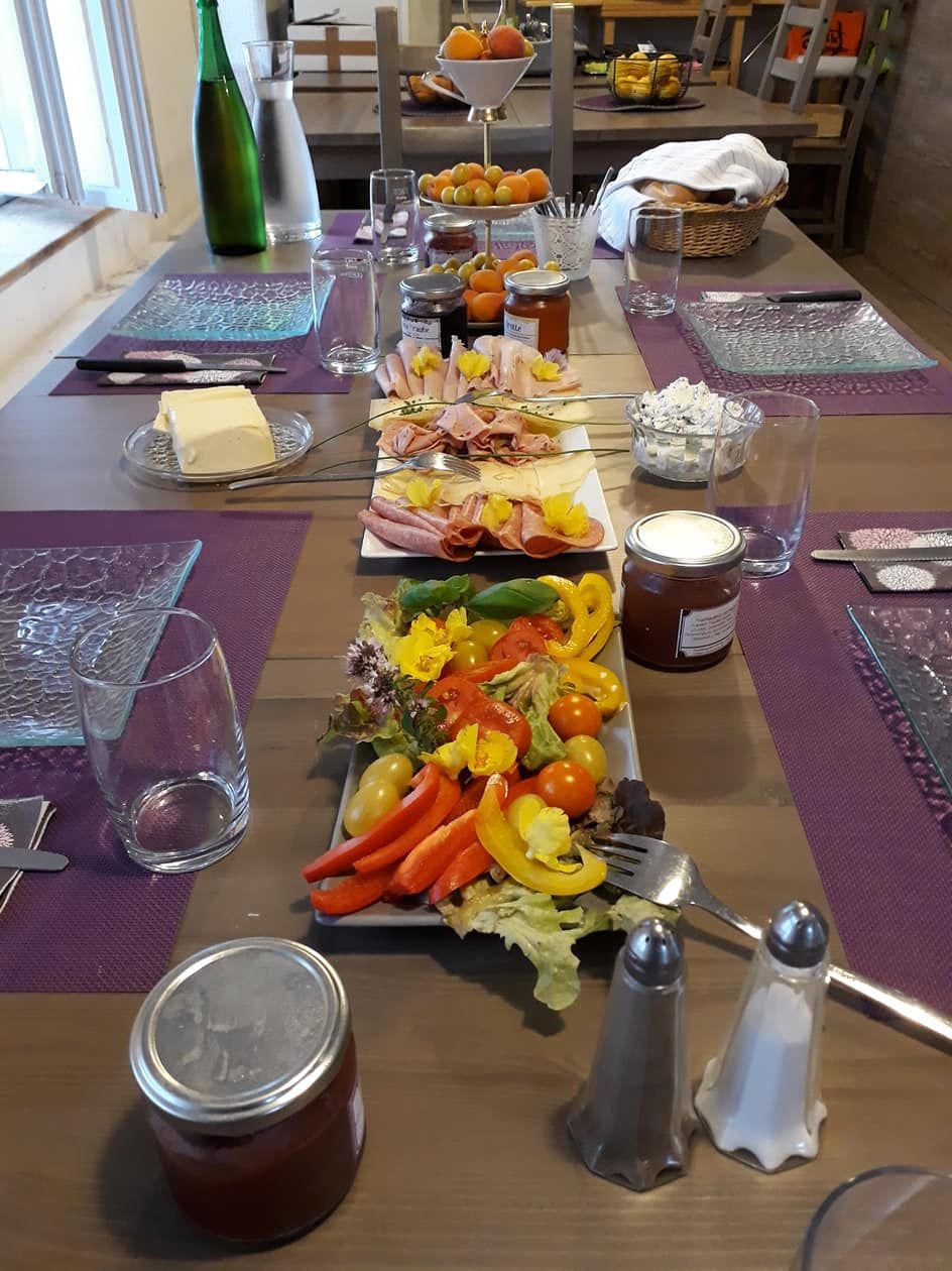 A laid breakfast table with cold cuts, vegetables, jam and drinks.