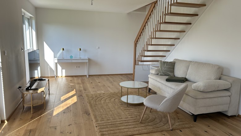 Modern living room with wooden staircase, sofa, armchair and coffee table on wooden floor.