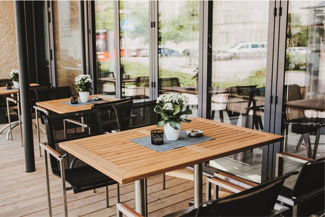 Terrace of a wine bar with wooden tables, chairs and flowers in pots.