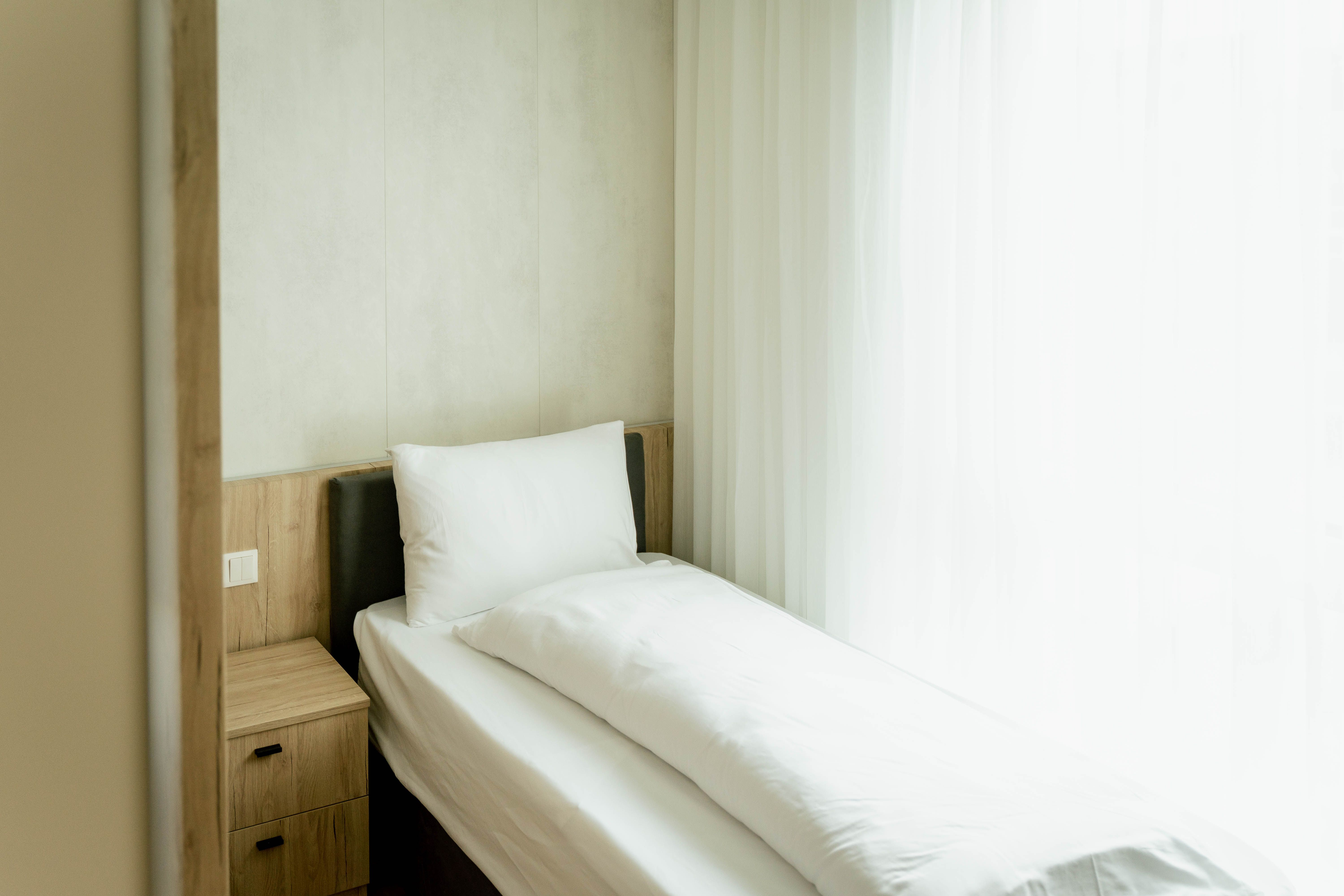 Single bed in a bright hotel room with white bed linen and a bedside table.