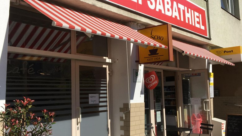 Exterior view of a bakery with red awnings and outdoor seating.